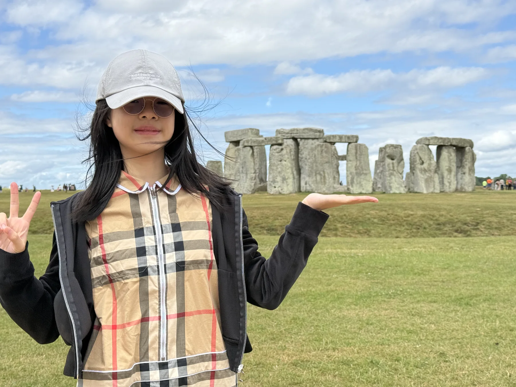 Angela smiling in front of Stonehenge and holding one hand beneath the stones